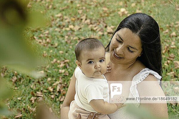 Portrait of attractive hispanic mother with her baby in a park. Baby looking at camera