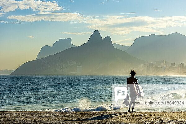 Boy with his bodyboard looking at the sea from Ipanema beach in Rio de Janeiro at dusk  Brasil