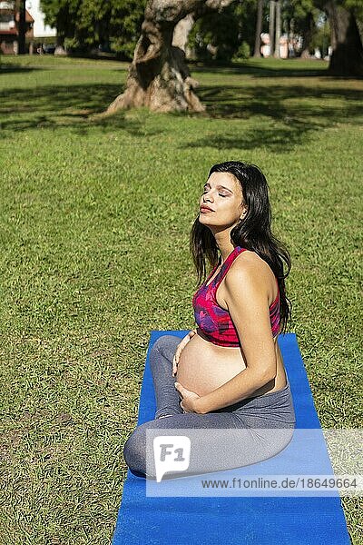 Schwangere lateinamerikanische Frau macht Yoga in einem Park