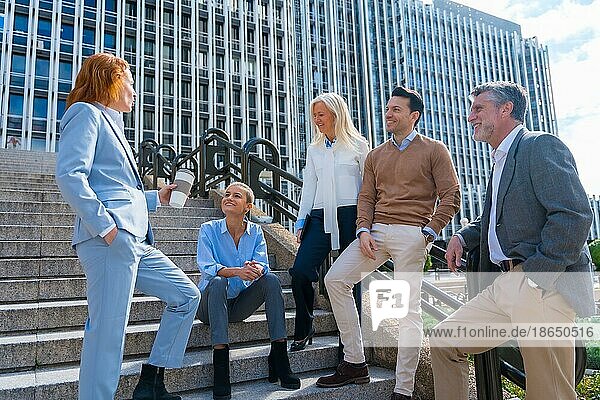 Cheerful group of coworkers outdoors in a corporate office area having a break time on the stairs