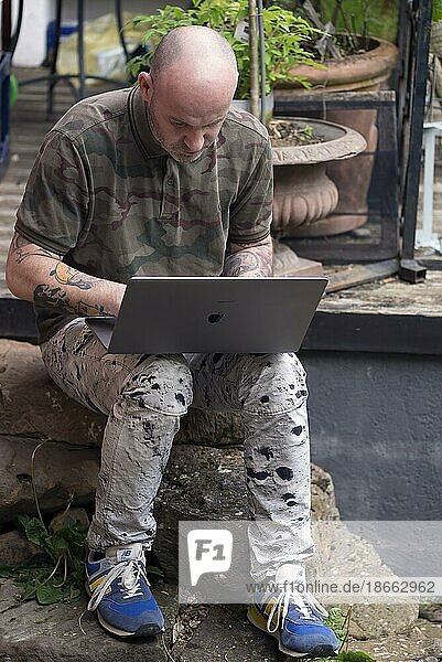 Man with tattooed arms works on laptop in home office in garden  Baden-Württemberg  Germany  Europe