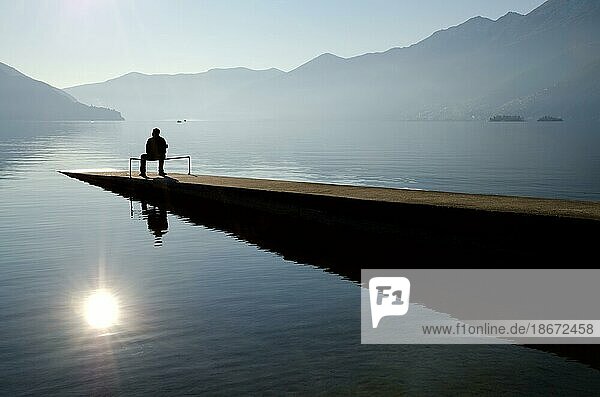 Mann sitzt auf dem Steg in der Nähe des Sees mit Berg im Tessin  Schweiz  Europa