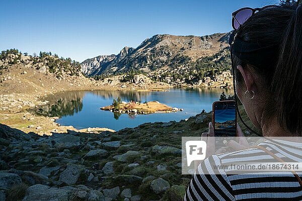 Woman taking a picture with her smartphone  Lake Estanh Plan  Circo de Colomers  Pyrenees  Lleida  Spain  Europe
