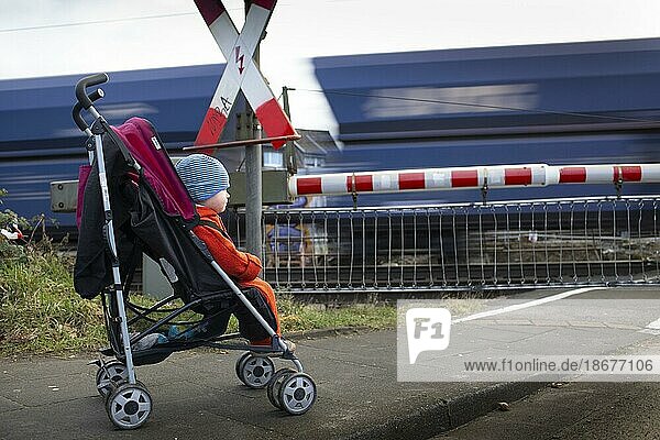 Thema: Verkehr. Kind im Kinderwagen vor einem Bahnübergang hinter dem ein Güterzug fährt  Bonn  Deutschland  Europa