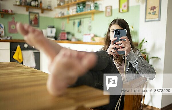 Thema: Mädchen sitz mit Füssen auf dem Tisch im Wohnzimmer und nutzt ein Handy