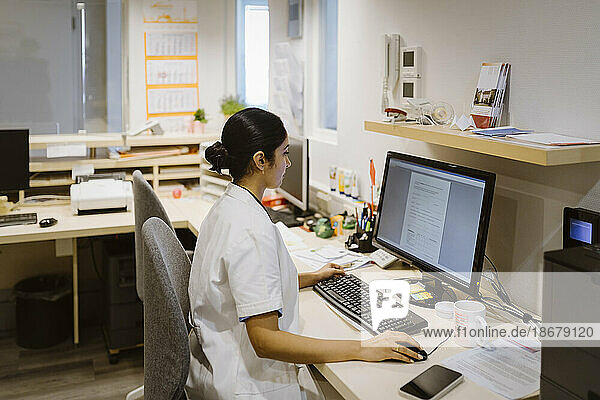 Side view of female healthcare worker using desktop PC at hospital