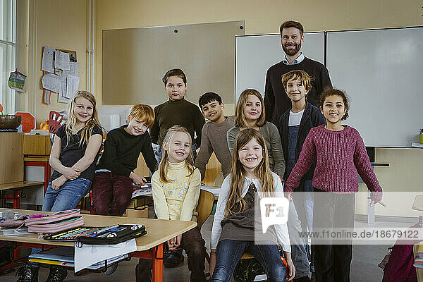 Porträt von lächelnden Lehrer und Mädchen und Jungen gegen Whiteboard im Klassenzimmer