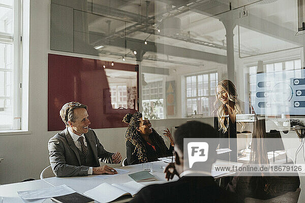 Happy male and female entrepreneurs during business meeting at office seen through glass