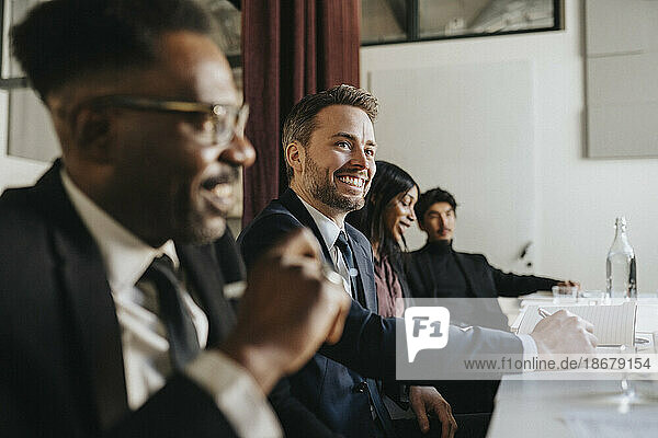 Lächelnder Geschäftsmann  der wegschaut  während er mit Kollegen bei einer Besprechung im Büro sitzt