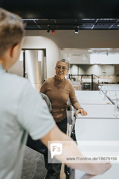 Ältere Frau diskutiert mit männlichem Verkäufer bei Waschmaschinen in einem Elektronikgeschäft