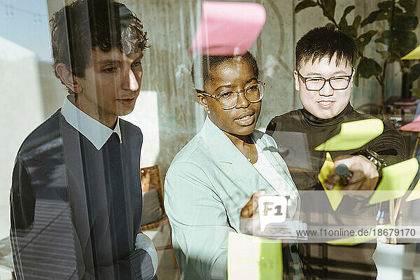 Multiracial male and female colleagues discussing over sticky notes in creative office