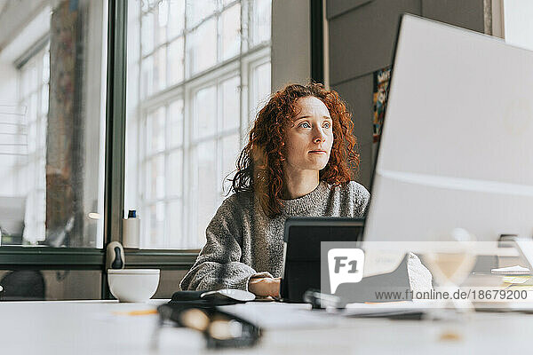 Konzentrierte rothaarige Geschäftsfrau  die im Büro an einem Desktop-PC arbeitet