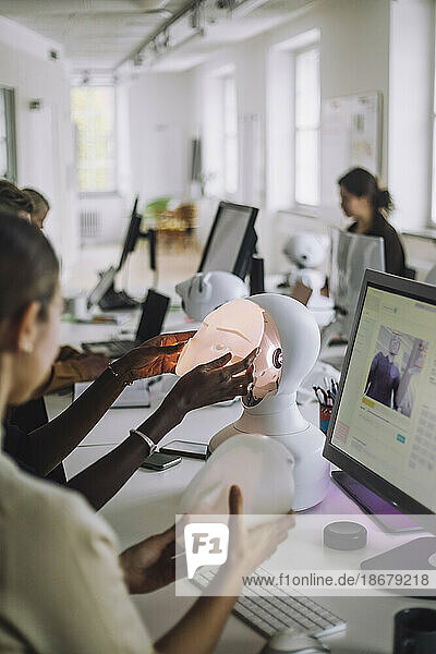 Multiracial students discussing over social robot at desk in innovation lab