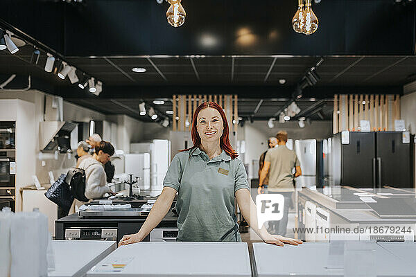 Portrait of smiling female sales clerk leaning on washing machine in electronics store