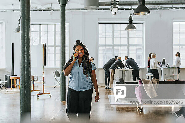 Nachdenkliche Geschäftsfrau  die beim Spazierengehen im Büro mit ihrem Smartphone telefoniert