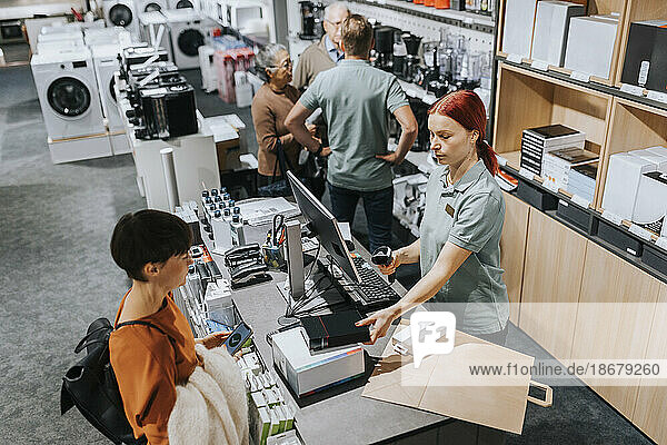 Ältere Frau an der Kasse stehend  während eine Verkäuferin Geräte im Laden scannt