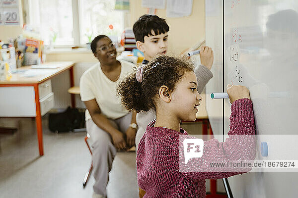 Mädchen und Junge schreiben auf der Tafel  während sie im Klassenzimmer mathematische Aufgaben lösen
