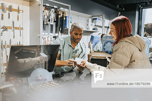 Männlicher Angestellter im Einzelhandel zeigt einer Kundin an der Kasse eines Elektronikgeschäfts die Rechnung