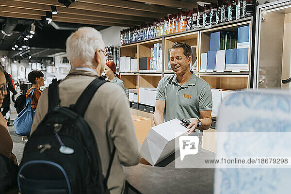 Ein lächelnder Verkäufer zeigt den Kunden an der Kasse eines Elektronikgeschäfts eine Gerätebox