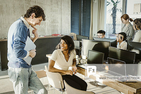 Multiracial programmers smiling while discussing in creative office