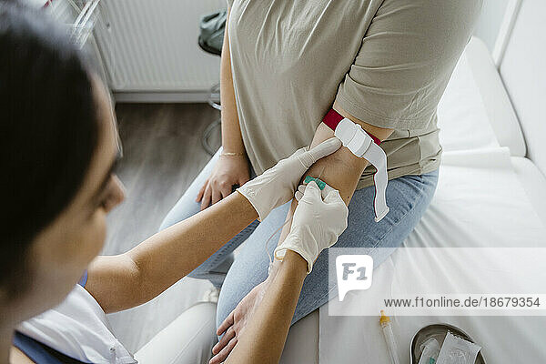 Arzt mit Handschuh sticht in der Klinik eine Nadel in den Arm eines Patienten