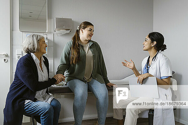 Female doctor explaining patient sitting with mother in clinic