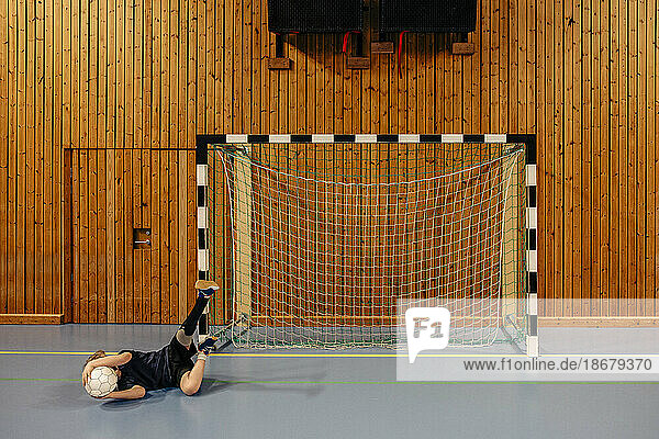 Männlicher Torwart mit behindertem Bein liegt auf dem Boden und hält einen Fußball  während er auf einem Sportplatz spielt