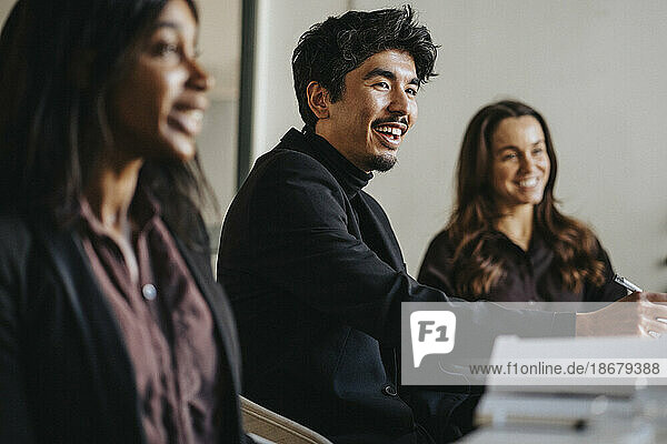 Lächelnder Geschäftsmann mit weiblichen Kollegen während einer Sitzung im Sitzungssaal im Büro