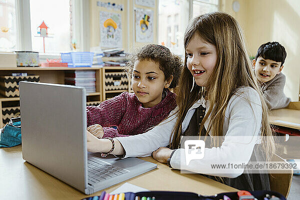 Schulmädchen benutzen gemeinsam einen Laptop am Schreibtisch im Klassenzimmer
