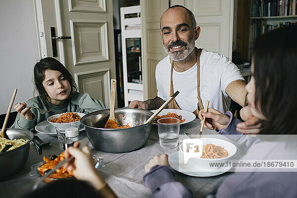 Glücklicher Vater isst Spaghetti mit Kindern am Esstisch