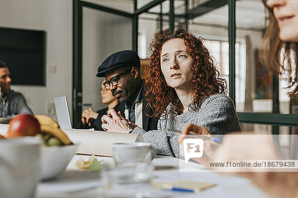 Rothaarige Geschäftsfrau sitzt mit Kollegen am Schreibtisch während einer Besprechung im Büro