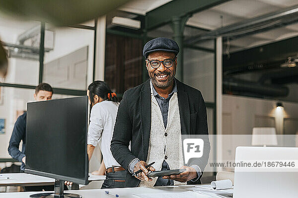 Porträt eines lächelnden Geschäftsmannes mit Tablet-PC  der an einem Schreibtisch im Büro steht