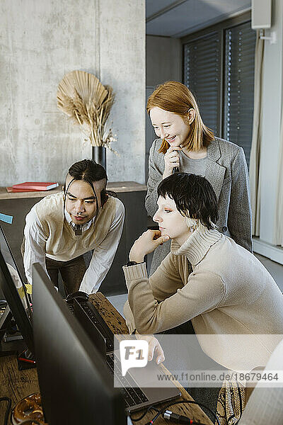 Smiling businesswoman with programmers looking at computer in startup office