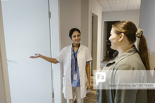 Lächelnder Arzt  der eine Patientin in den Untersuchungsraum einer Klinik begleitet