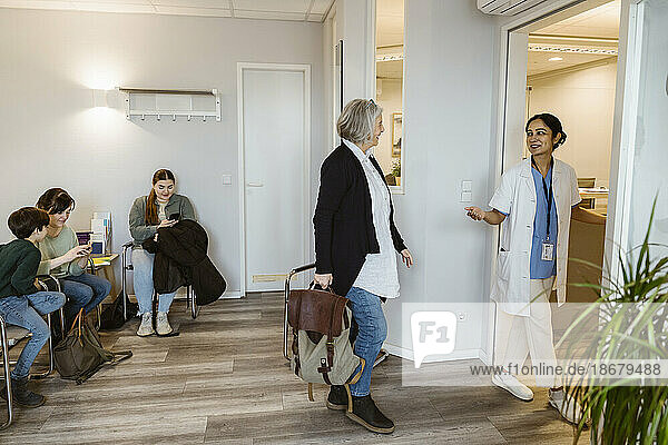 Ältere Patientin geht in Richtung Untersuchungsraum mit Arzt in der Klinik