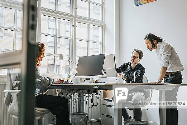 Businessmen discussing over desktop PC at desk in office