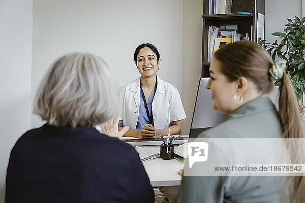 Lächelnde Ärztin hört einem älteren Patienten mit Tochter in der Klinik zu