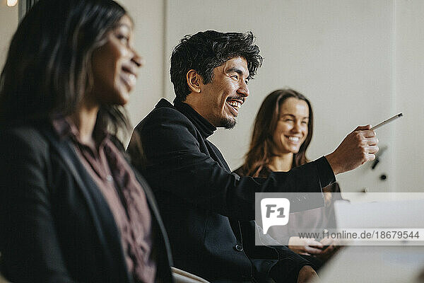 Happy male entrepreneur pointing during business meeting with female colleagues at office