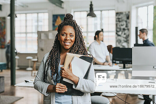 Portrait of smiling businesswoman with braided hair holding files at office
