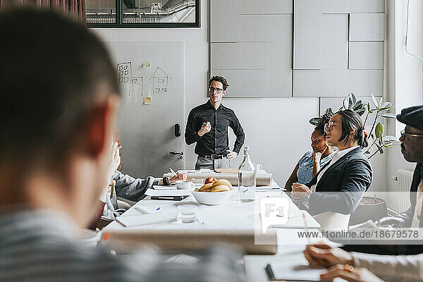Businessman with hand on hip discussing with colleagues during meeting at office