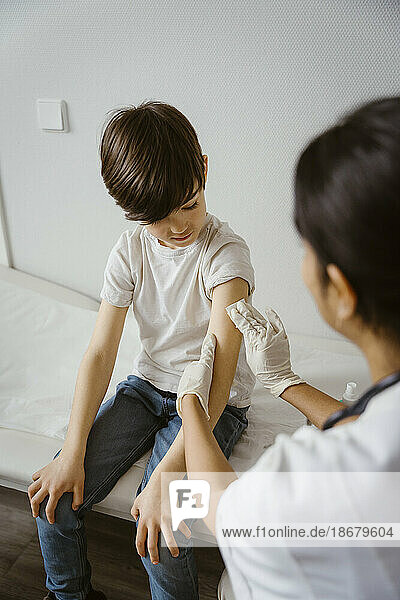 Kinderarzt reinigt den Arm eines Jungen mit einem Alkoholtupfer im Gesundheitszentrum