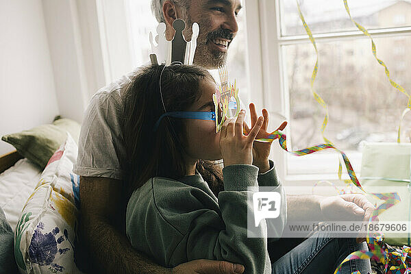 Mädchen mit Krone und Brille genießt mit Band  während sie auf Vater zu Hause sitzt