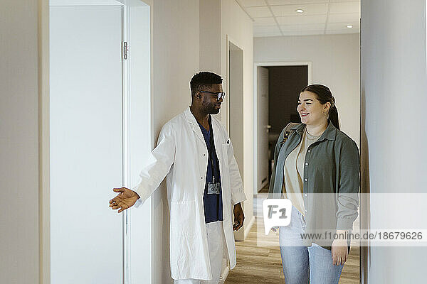 Krankenpfleger  der einer Patientin beim Betreten des Sprechzimmers im Krankenhaus hilft