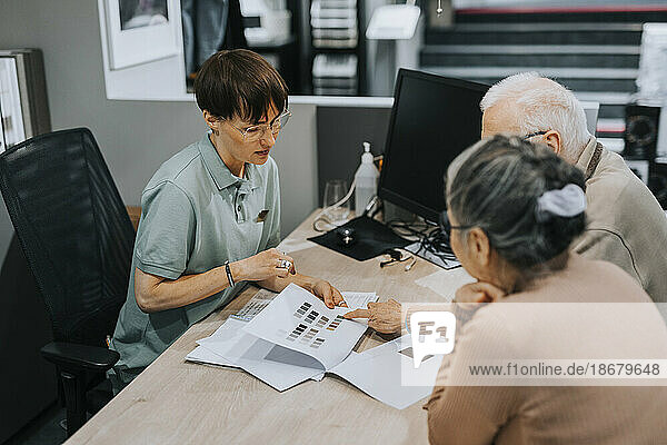 Ein älteres Paar diskutiert mit einer Innenarchitektin über eine Broschüre am Schreibtisch in einem Geschäft