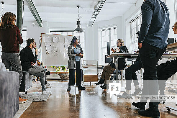 Gemischtrassige Kollegen hören einer Geschäftsfrau zu  die bei einem Treffen im Büro ihre Strategie erläutert