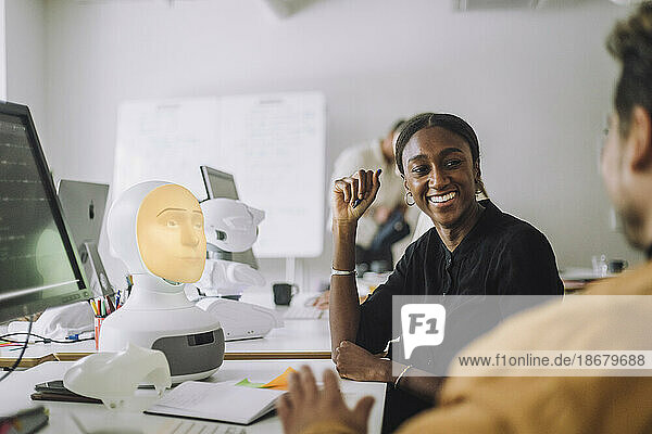 Smiling female PhD student discussing with man at desk in innovation lab