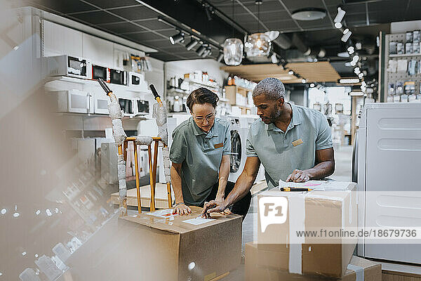 Multiracial male and female colleagues discussing over box while working in electronics store