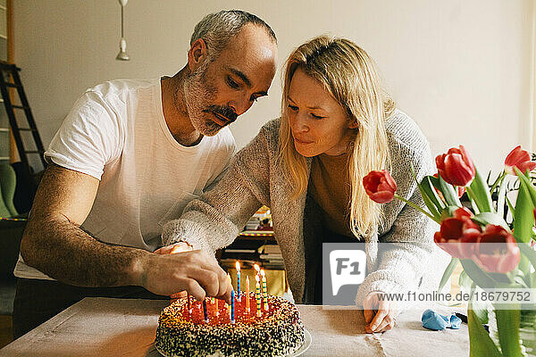 Paar arrangiert Kerzen auf Geburtstagskuchen zusammen zu Hause