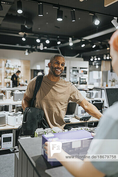 Smiling mature man talking with sales clerk at checkout counter in appliances store