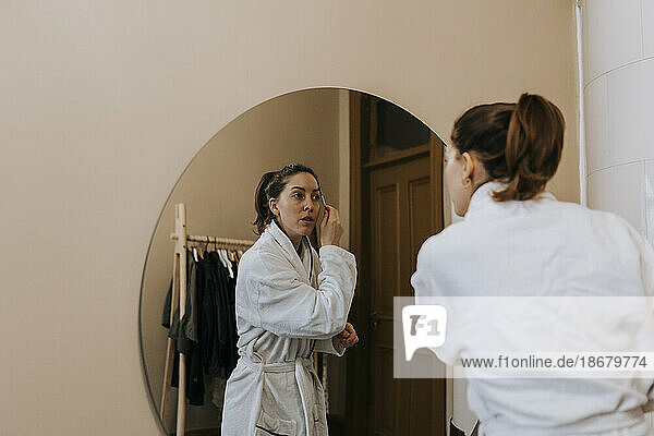 Nicht-binäre Person  die einen Augenbrauenstift benutzt  während sie sich zu Hause im Spiegel betrachtet